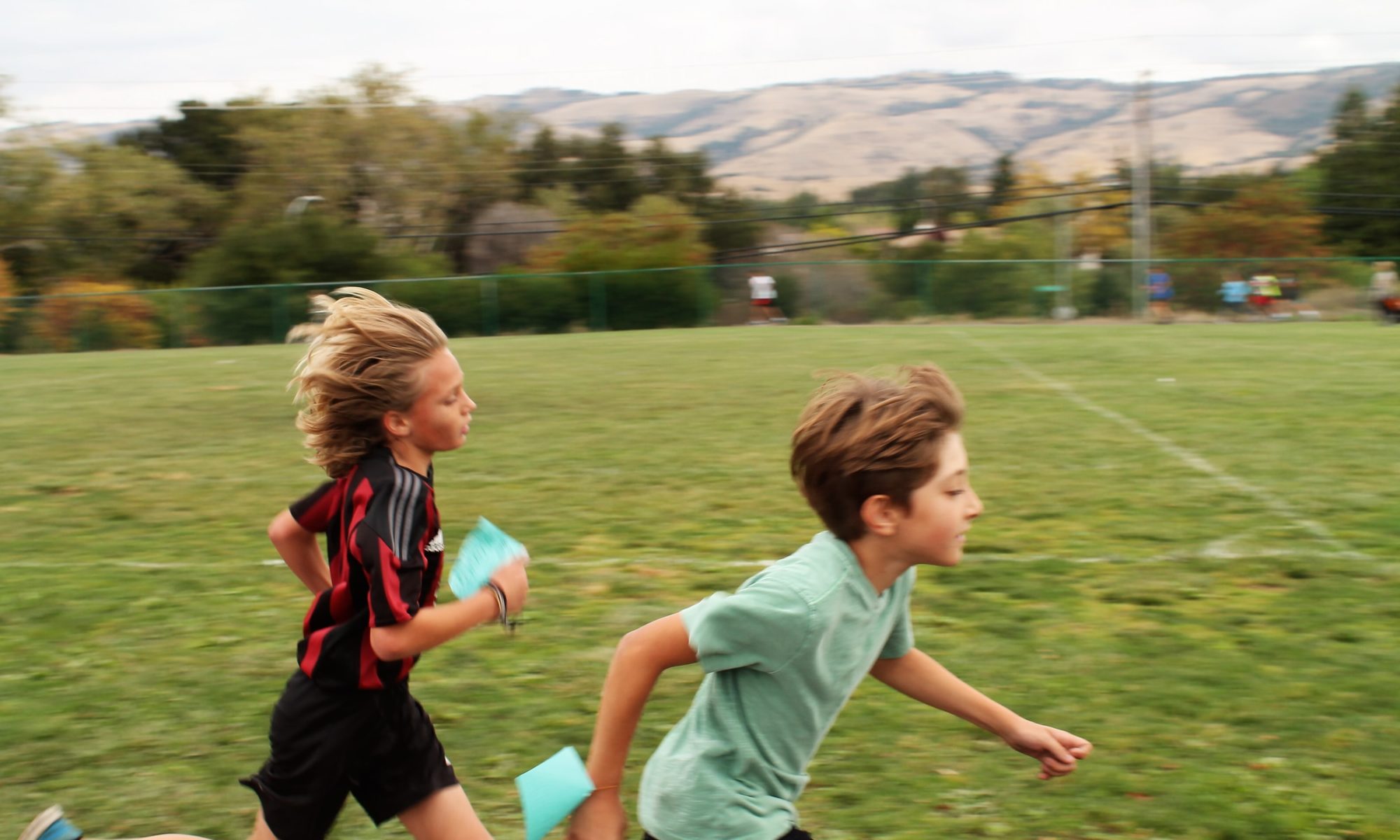 Two children run together on a field.