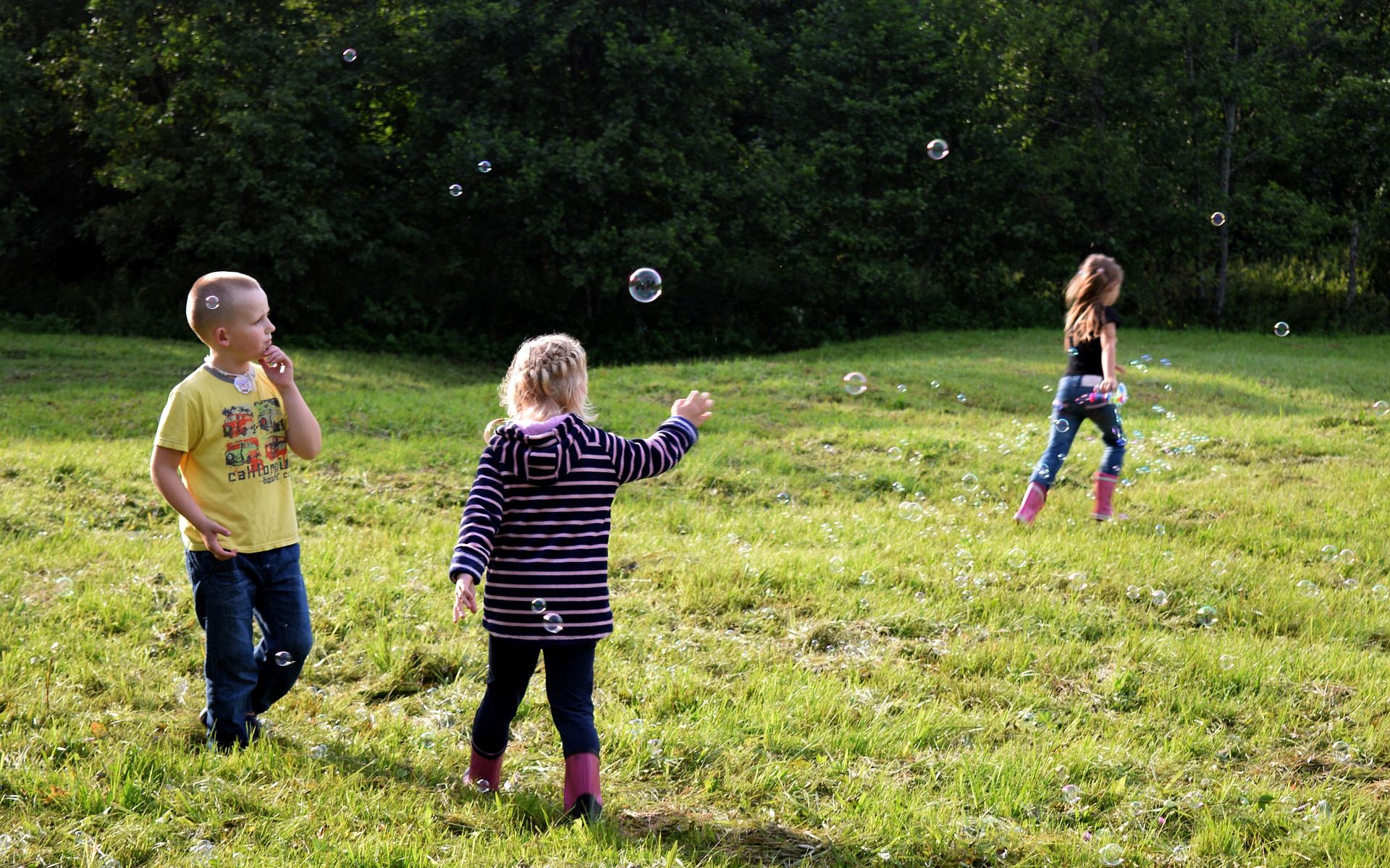 Three kids play with bubbles in the backyard.